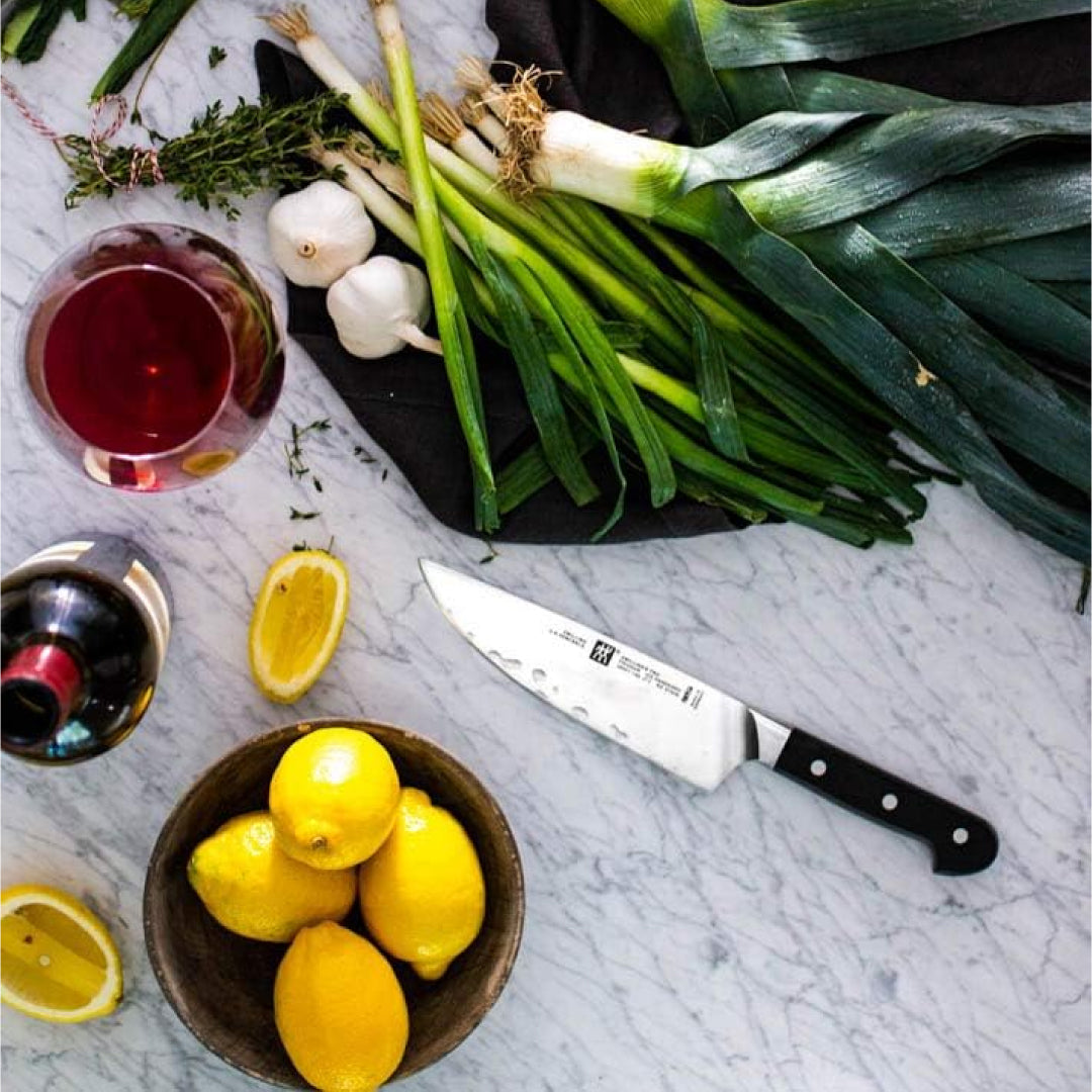 Zwilling Pro chef’s knife lying on a marble countertop surrounded by fresh vegetables, lemons, garlic, and wine